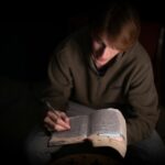 a man sitting in a chair holding a book and a pen
