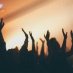 A crowd of people with arms raised in a dimly lit concert venue